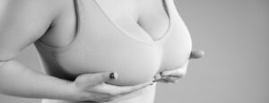 Close-up of a person wearing a bra cupping their breasts with both hands for support.