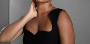 Close-up of a woman wearing a black sleeveless dress, touching her neck with her hand.