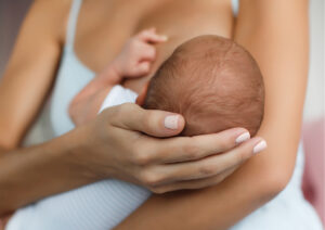 Mother gently cradles a newborn baby in her arms, supporting the baby's head with both hands.