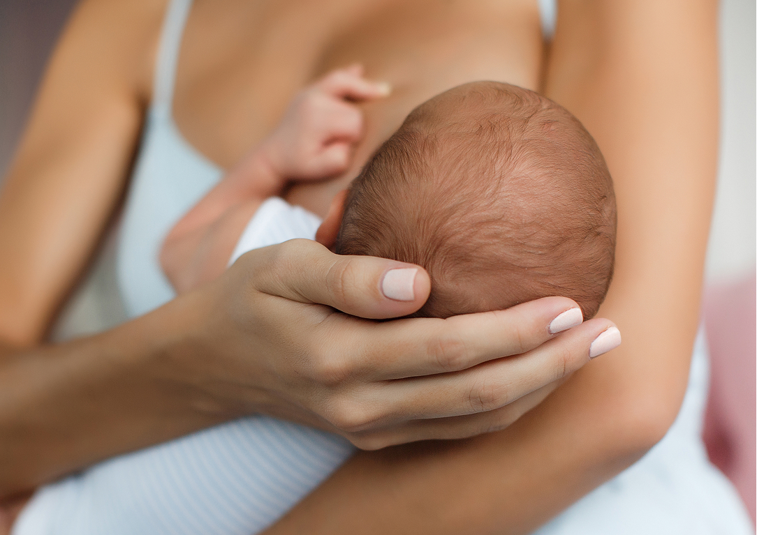 Mother gently cradles a newborn baby in her arms, supporting the baby's head with both hands.