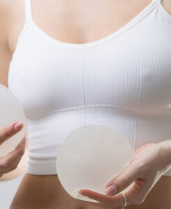 Person in a white sports bra holds two round silicone breast prostheses in each hand, likely for mastectomy reconstruction