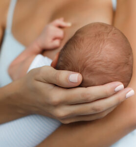 Mother cradling a newborn baby's head in her hands, face not visible.