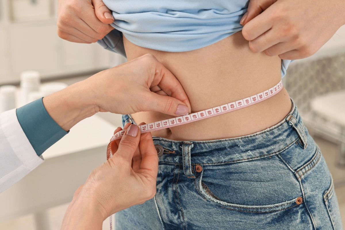 img-How-Much-Does-Liposuction-Cost-by-Treatment-Area-in-Dallas-Fort-Worth | Geo N. Tabbal, M.D. Healthcare professional measures a person’s waist with a tape measure during a health checkup.
