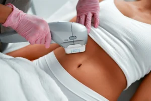 Clinician in pink gloves applying a body-contouring device to a woman's bare abdomen during a cosmetic procedure.