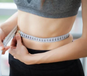 Person wraps a measuring tape around their bare midsection, checking waist size for fitness tracking.