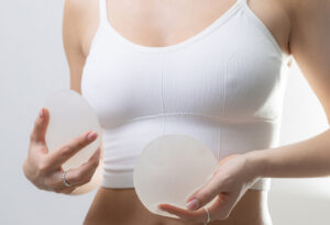 Person in a white sports bra holds two round silicone breast implants in each hand.